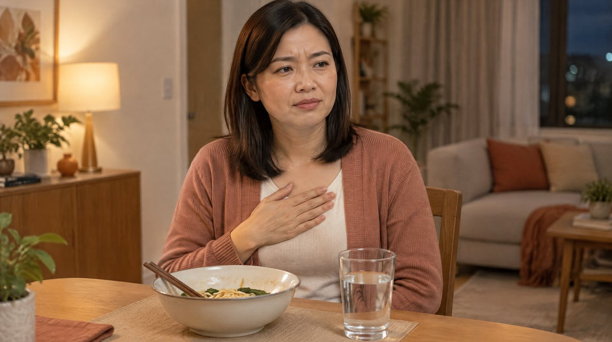 A woman at the dinner table with a hand on her chest from heartburn