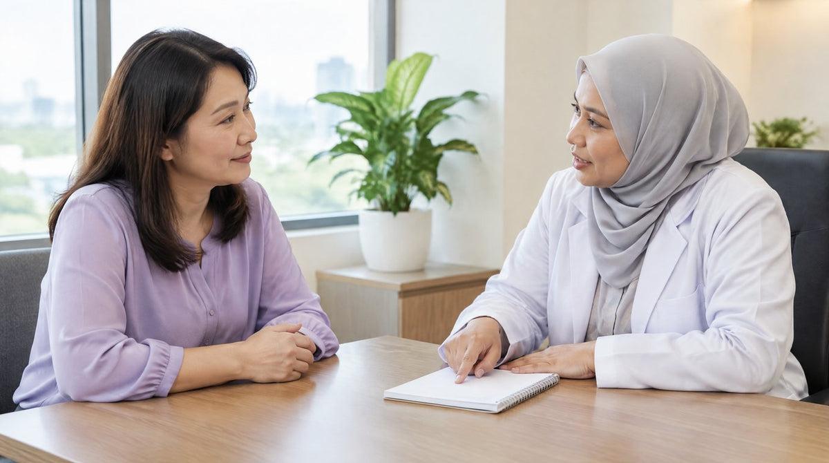 A woman listening to a female doctor in a hijab and white coat explaining something at a clinic desk