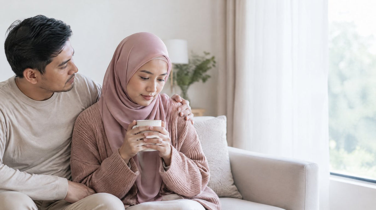 A husband comforting his wife on a sofa as she holds a warm drink