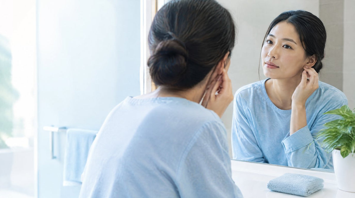 A woman touching her earlobe while looking in a bathroom mirror