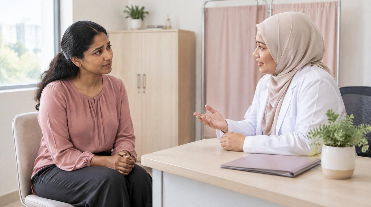 A woman talking with a female doctor in a hijab across a desk in a calm clinic consultation room