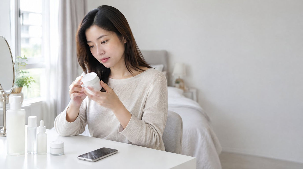 A woman at her dressing table carefully reading the label on a plain skincare jar