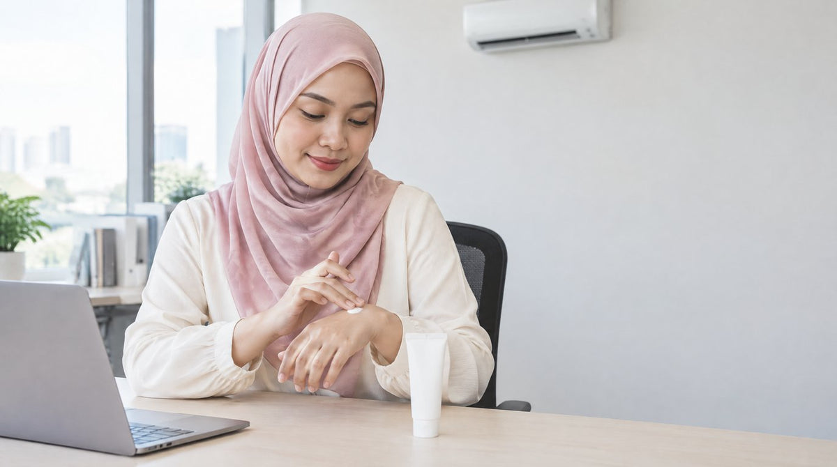 A woman in a hijab applying moisturising cream to the back of her hand at her office desk