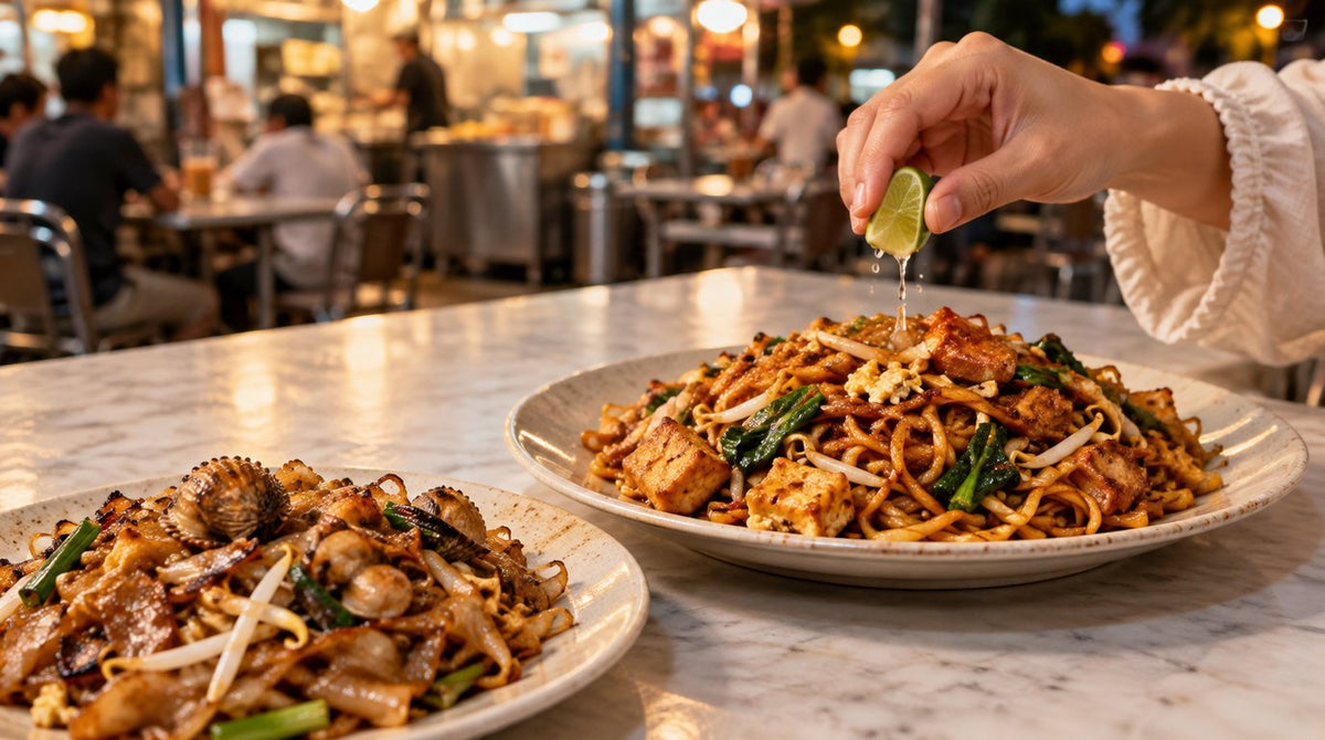 A plate of mee goreng mamak with tofu, choy sum and bean sprouts beside a plate of char kuey teow with cockles at a Malaysian mamak restaurant