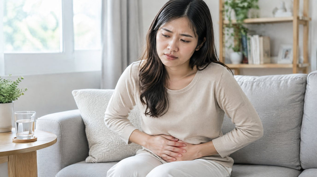 A woman sitting on a sofa holding her lower abdomen with a glass of water beside her