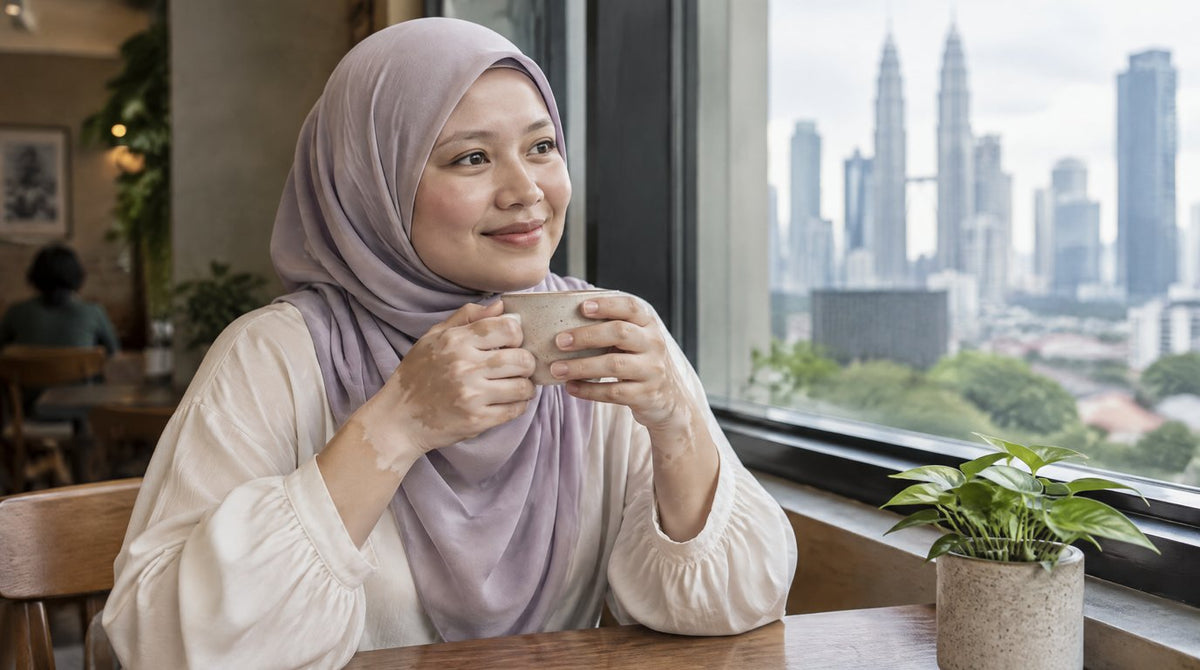 A smiling woman in a hijab holding a cup of tea, with lighter patches of skin on her hands